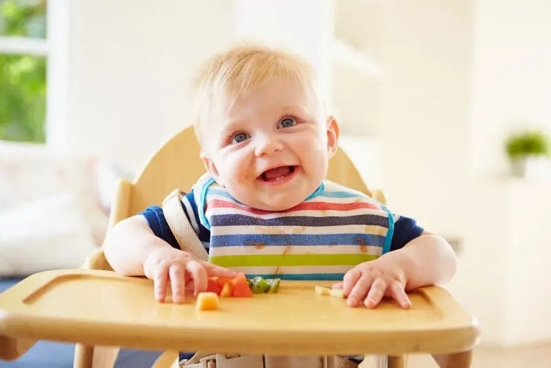 A toddler eating fruits on a high baby chair